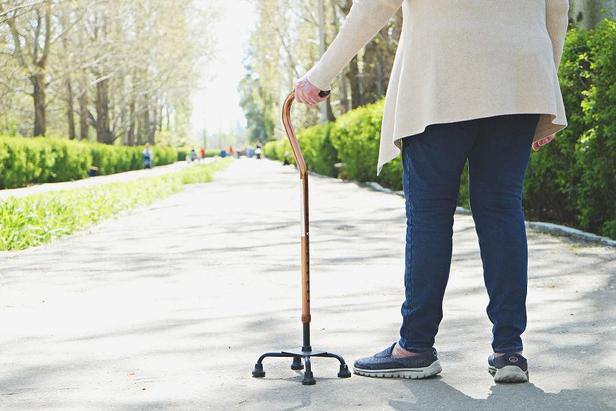 A woman uses a walking cane to walk down a pedestrian road.
